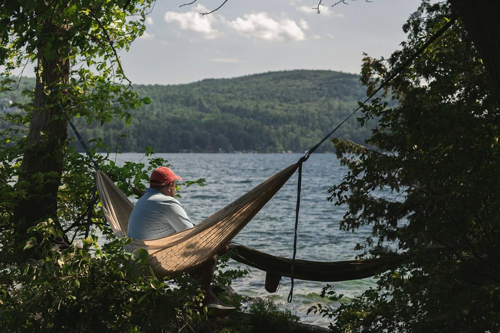 A man sitting in a hammock on the shore of a lake