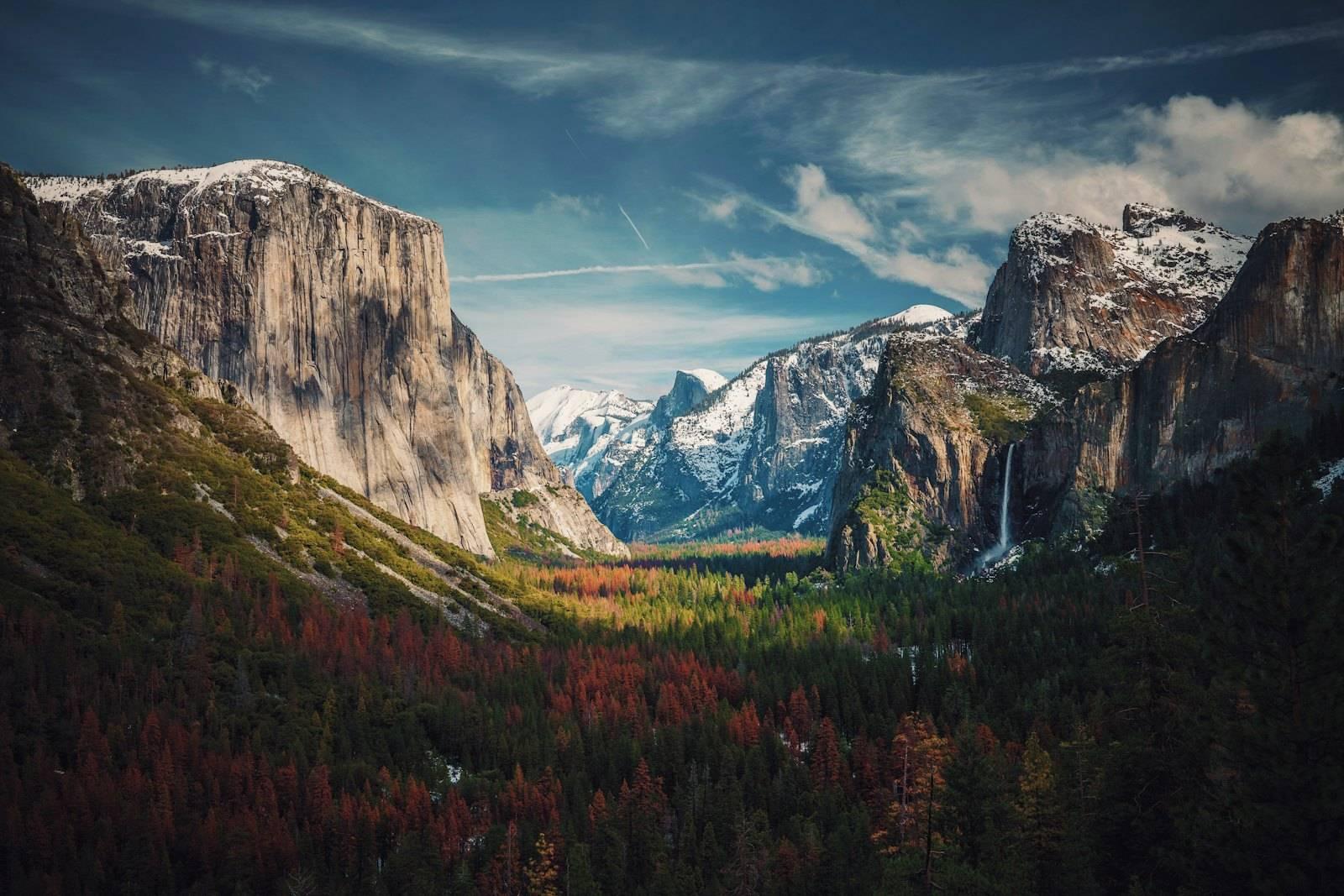 Snow-dusted granite cliffs and a waterfall above a forest in Yosemite National Park