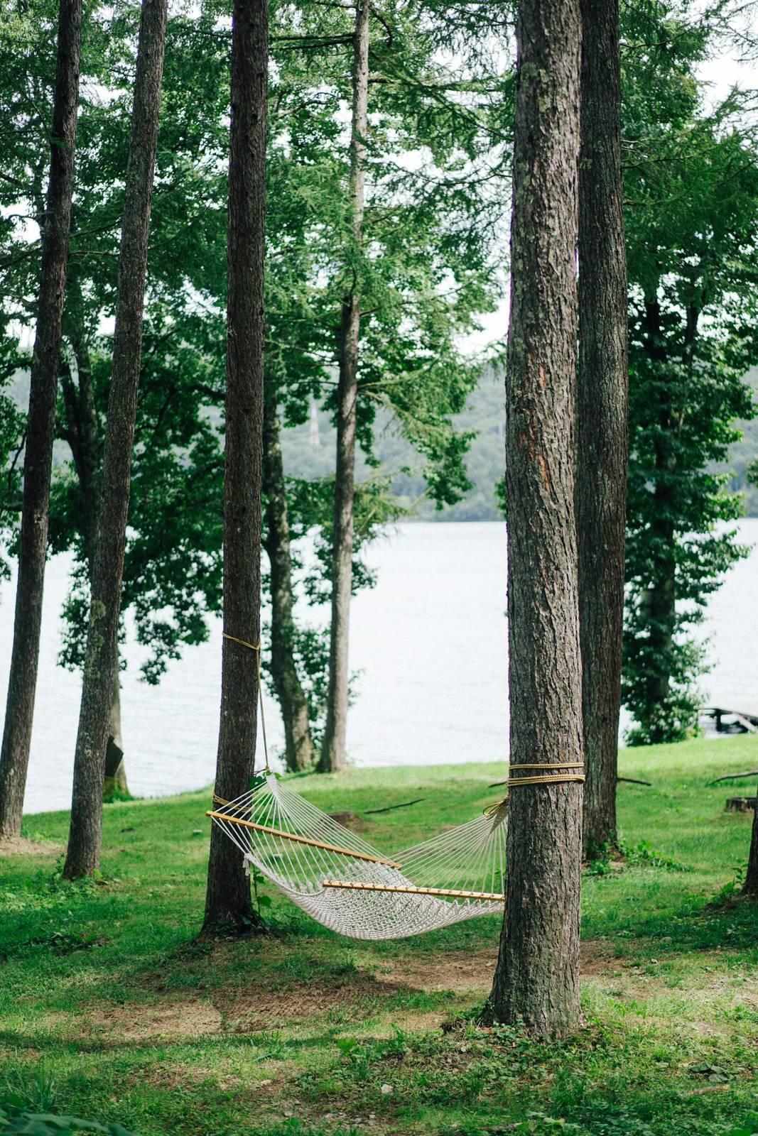 Green hammock tied on tree trunk near body of water during daytime